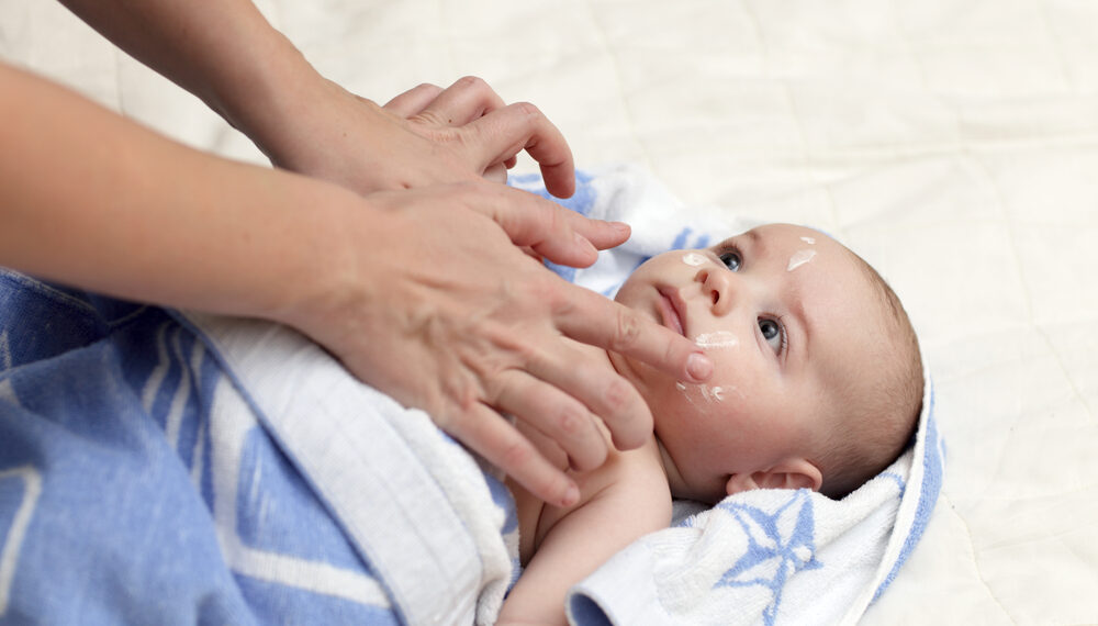 Baby liegt in einem Schlafsack auf dem Rücken und wird eingecremt.