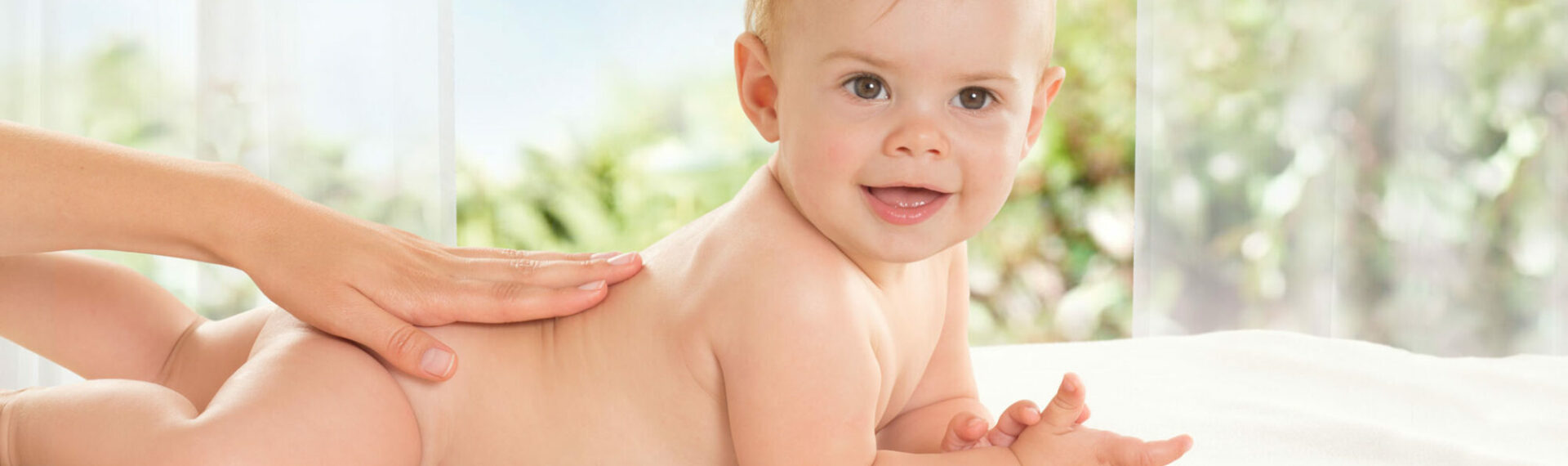 Ein Baby liegt auf dem Rücken und schaut verzückt in die Kamera, eine Hand streichelt ihm über den Rücken.