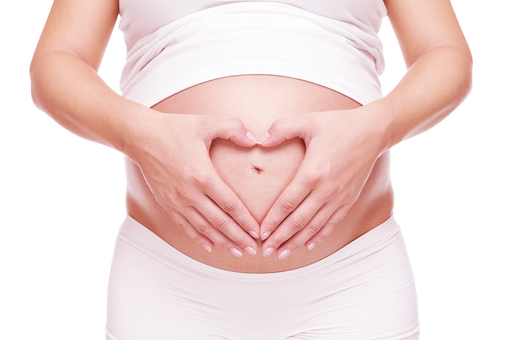 Schwangere Frau macht Herzform mit den Händen auf ihrem Bauch