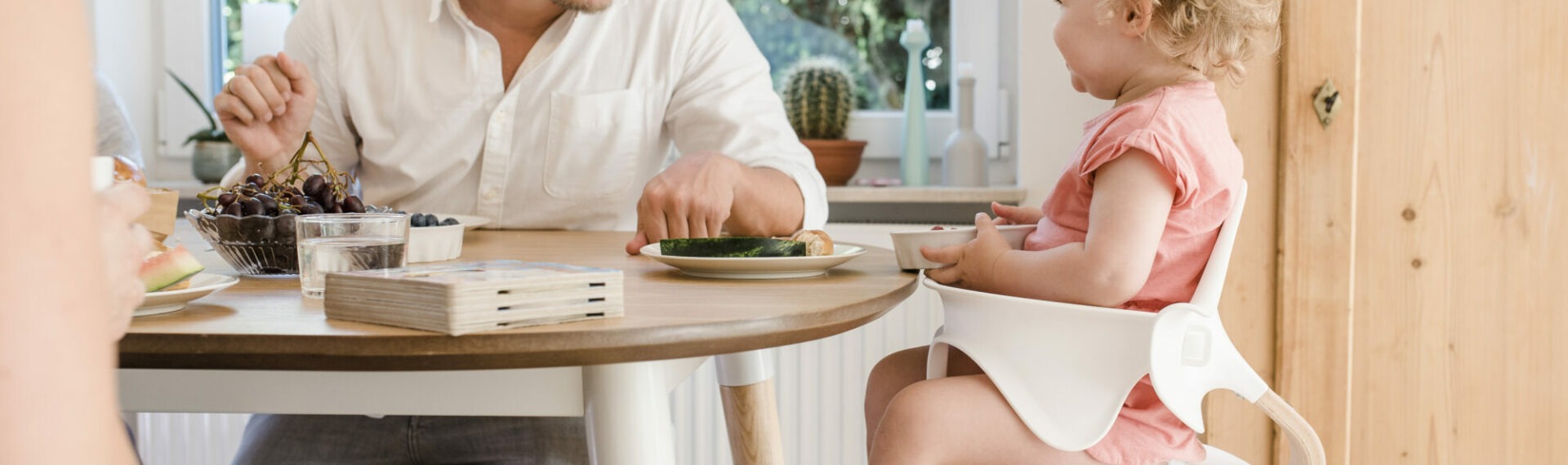 Vater lacht Tochter an, die im Evomove Nomi Hochstuhl sitzt
