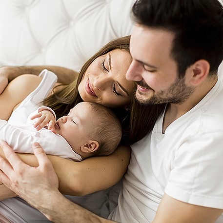 Papa, Mama und Baby kuscheln und lachen auf weißem Baby