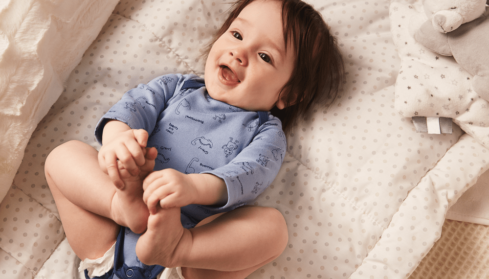 Lachendes Baby mit C&A Baby Body liegt lachend auf dem Rücken und fasst sich an die Füße