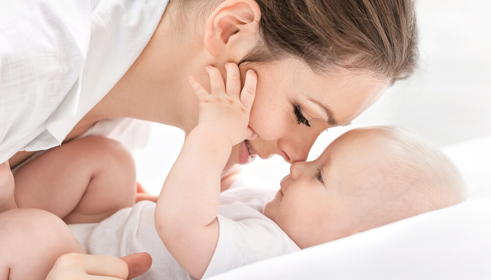 Lächelnde Mama lehnt sich über ihr Baby und gibt ihm einen Nasenkuss