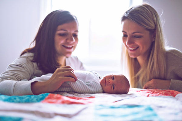 Zwei Frauen schauen lachend ein liegendes Baby an