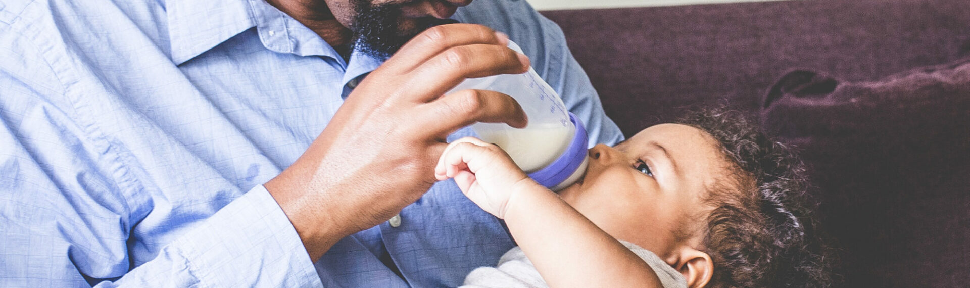Vater hält sein Baby auf dem Arm und füttert es mit einer Lansinoh Weithalsflasche