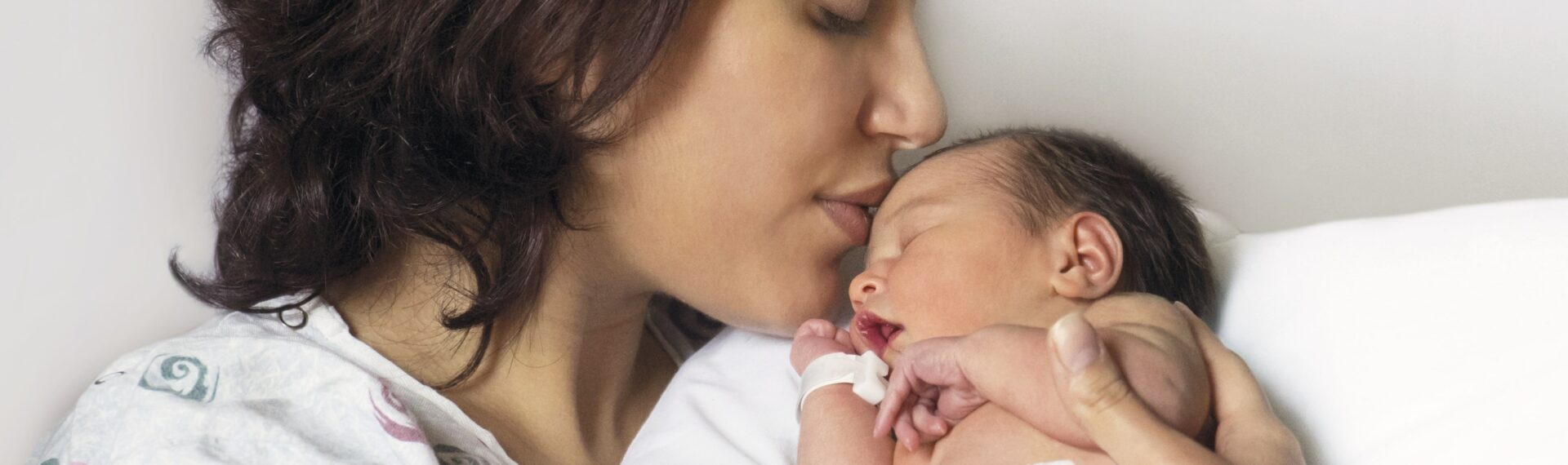 Mütter küsst Neugeborenes in ihrem Arm, das eine Pampers Premium Protection Windel trägt.