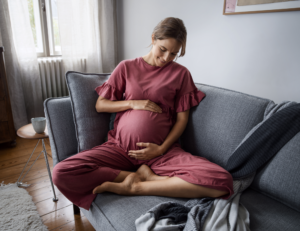 Schwangere Frau in rotem Overall hält ihren Bauch