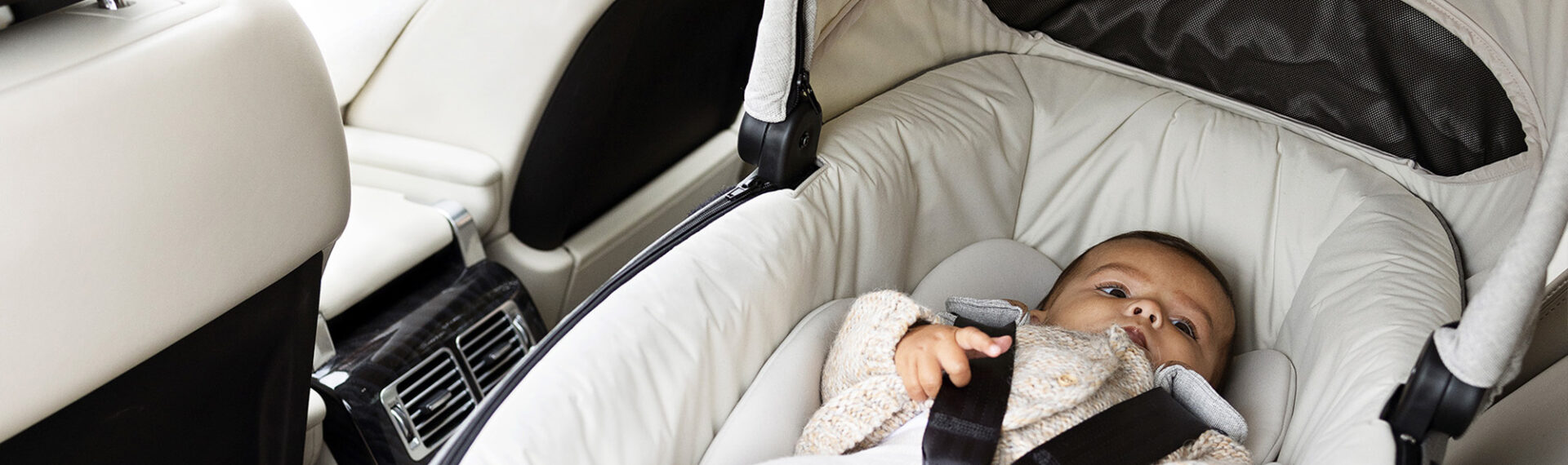 Mutter auf dem Fahrersitz ihres Autos, die über die Schulter auf ihr Baby in der Calmi R129 blickt