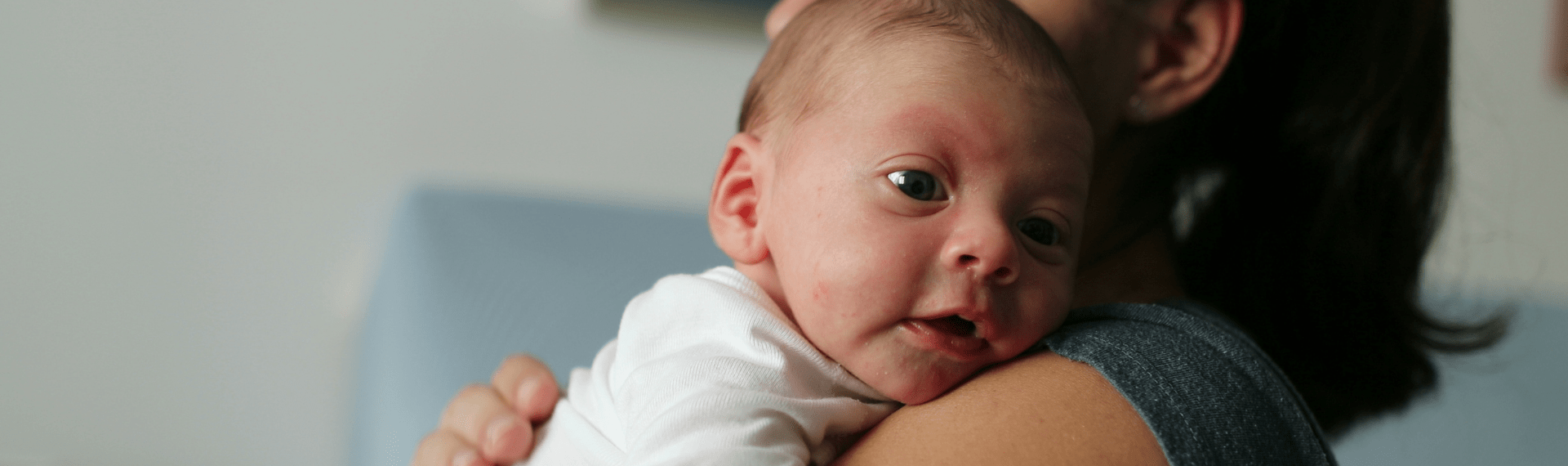 Mutter hält ihr Baby sanft und klopft ihm auf den Rücken, um Schluckauf beim Baby zu beruhigen.